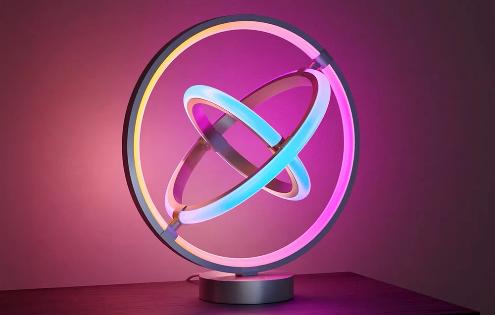 O lampă de birou formată din trei cercuri neon luminoase, așezată pe o masă de culoare închisă.