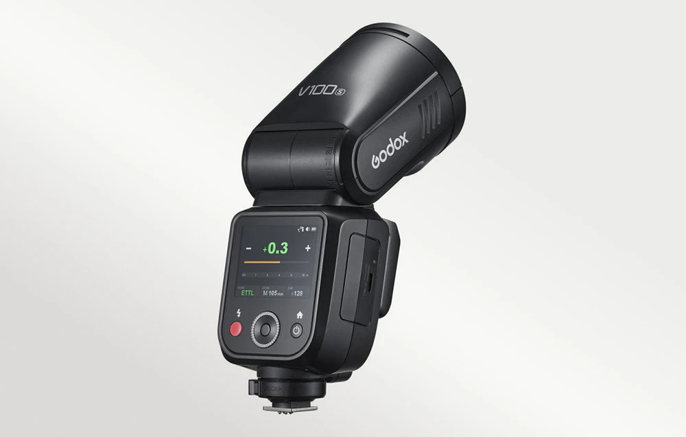 O unitate de bliț neagră cu un ecran de afișare care prezintă parametrii și logo-ul producătorului, privită din lateral și din spate, sub un unghi.