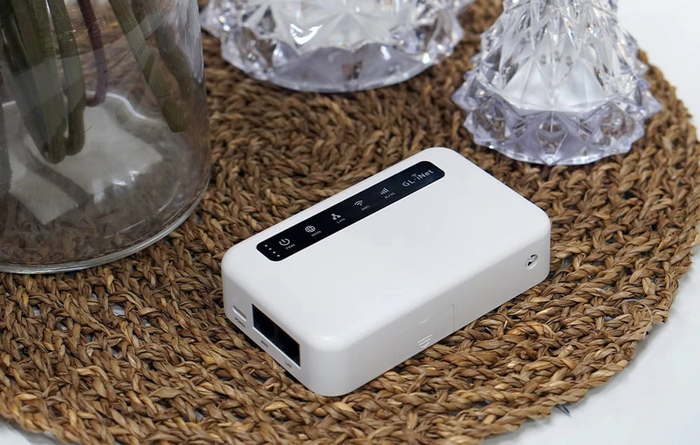 Un router alb așezat pe o rogojină rotundă din paie; porturile WAN și LAN laterale sunt vizibile.