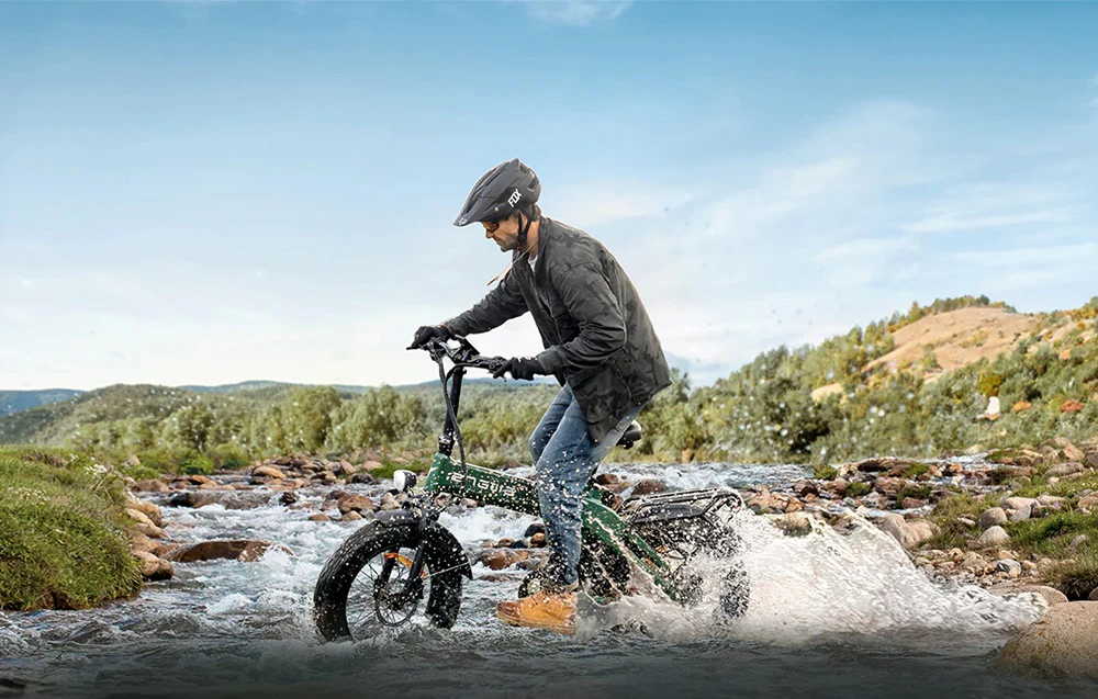 Un bărbat conduce o bicicletă electrică pliabilă verde printr-un pârâu puțin adânc