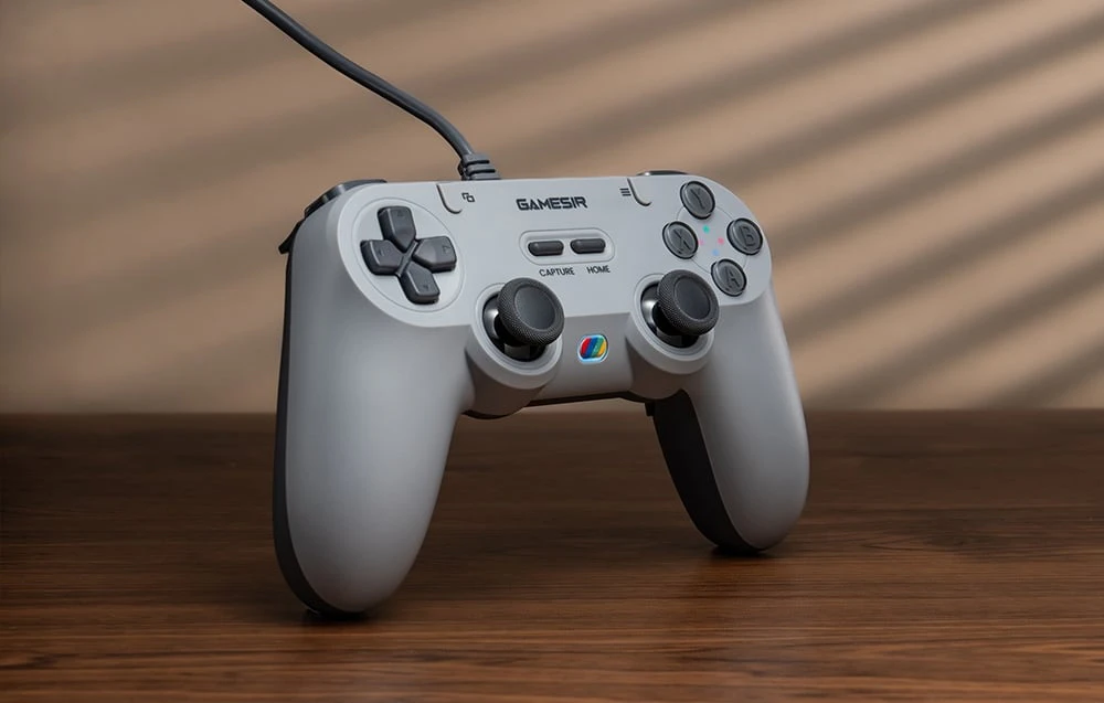Controler GameSir gri care stă vertical pe o masă de lemn, cu butoane vizibile și iluminare de fundal.