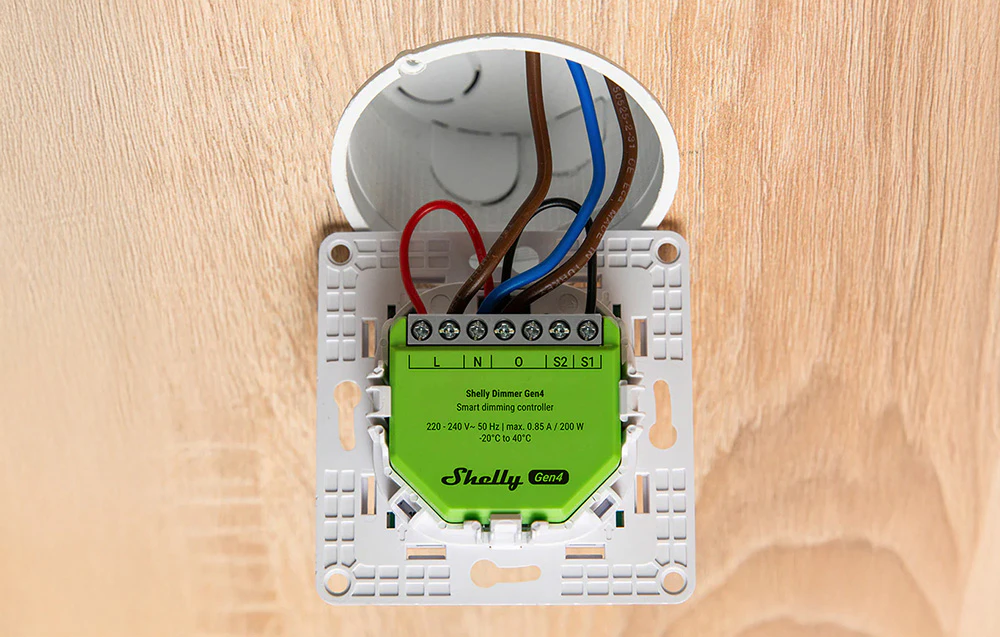 Un controler de iluminat verde instalat în perete, cu fire colorate conectate în interiorul cutiei de montare.