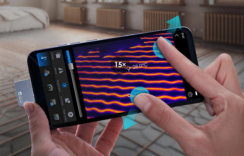 Mâinile măresc ecranul smartphone-ului pentru a mări imaginea termică a sistemului de încălzire prin pardoseală, marcată cu 15x și 26,0 °C
