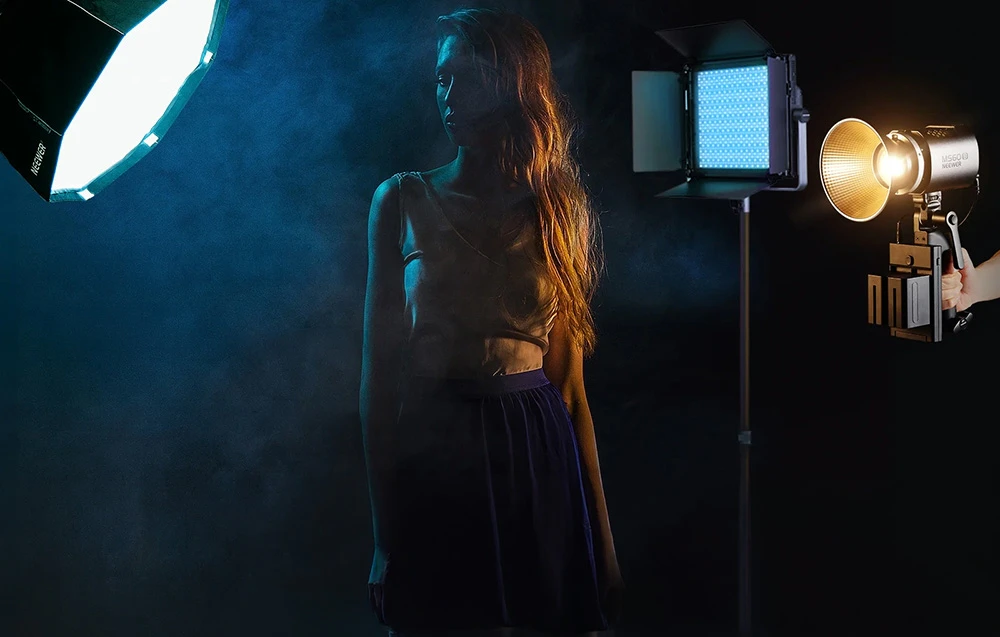 O femeie într-un studio întunecat, iluminată din lateral de trei lumini de fotografie diferite.