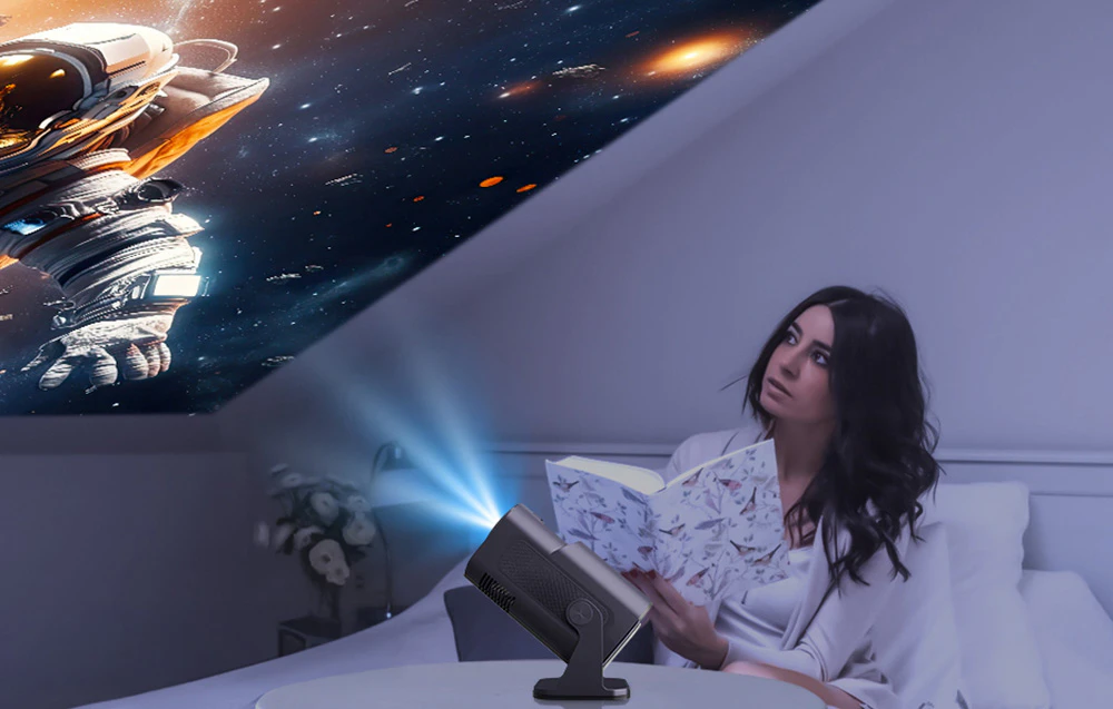 O femeie așezată pe un pat cu o carte deschisă privește tavanul, unde un proiector afișează imaginea unui astronaut în spațiul cosmic