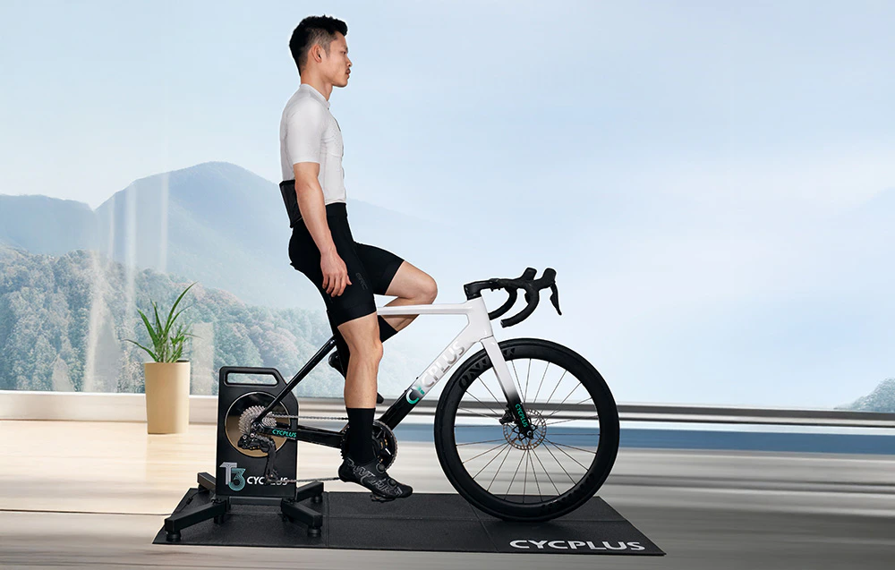 O persoană pe un trainer Cycplus T3 la o fereastră panoramică cu vedere la munți