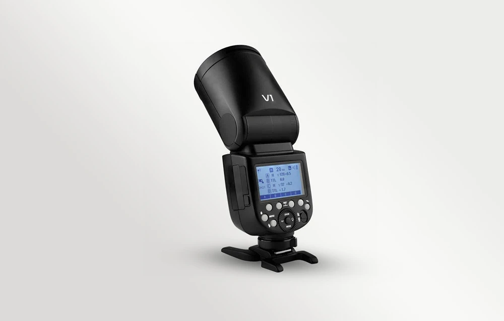 Blițul Godox V1 pe un stativ, cu ecranul LCD aprins și capul rotund înclinat într-o parte
