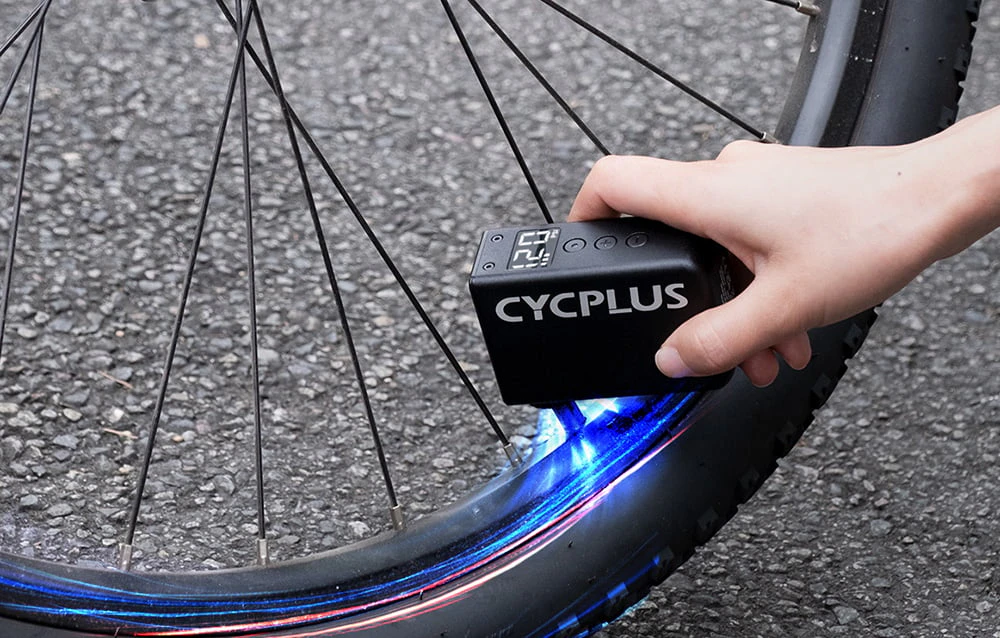 Mână care ține umflatorul Cycplus cu lumină albastră la roata motocicletei