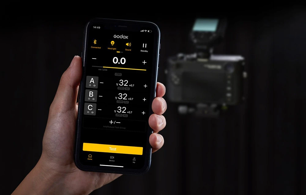 Un smartphone cu aplicația Godox Flash deschisă pentru controlul blițurilor, ținut în mână pe fundalul unui aparat foto