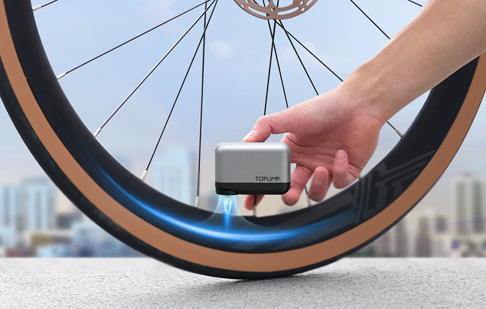 O mână care ține mini-pompa lângă o supapă de bicicletă în timp ce umflă o anvelopă în aer liber.