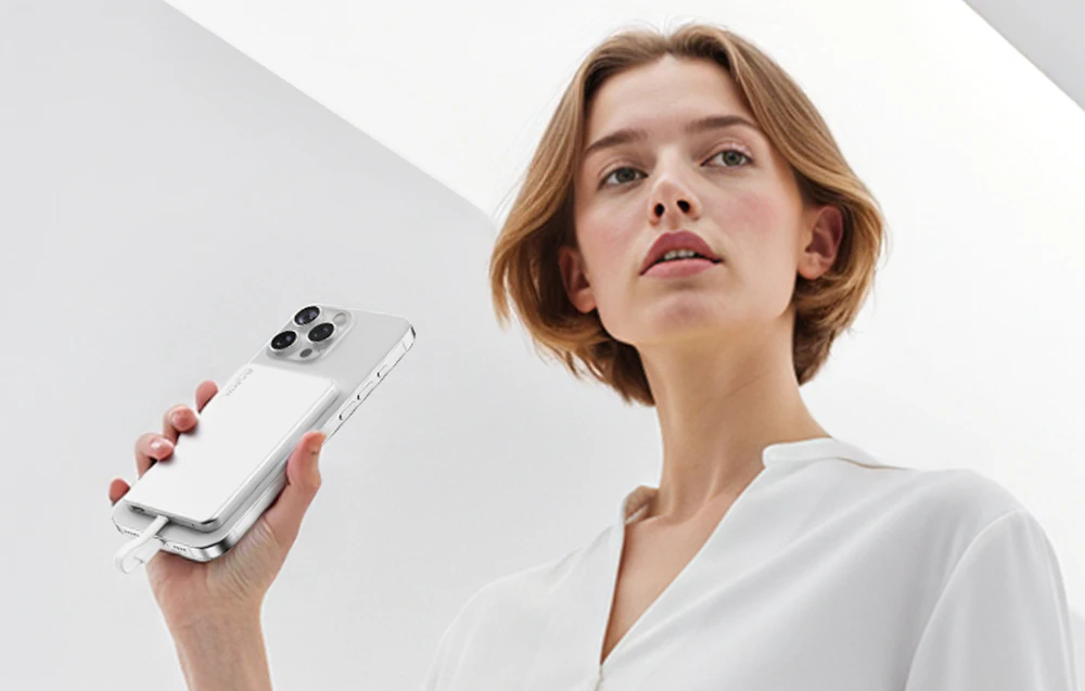 O femeie ține în mână un smartphone cu o baterie externă magnetică FlexTail atașată pe partea din spate a dispozitivului.