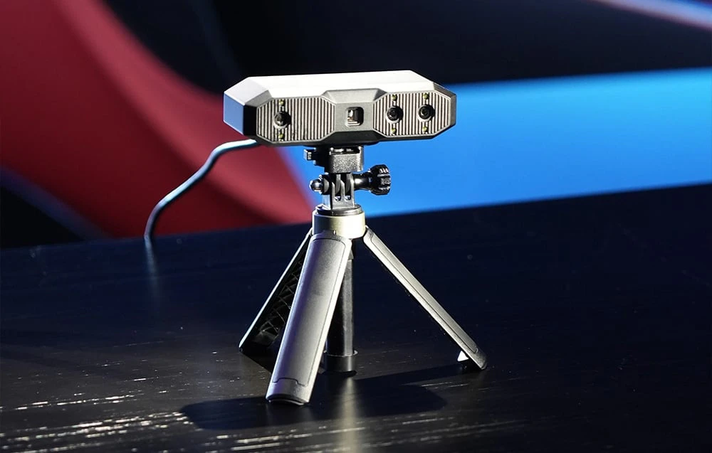 Scannerul 3D Revopoint Mini 2 pe un trepied, cu trei lentile și un cablu de alimentare vizibile în spate