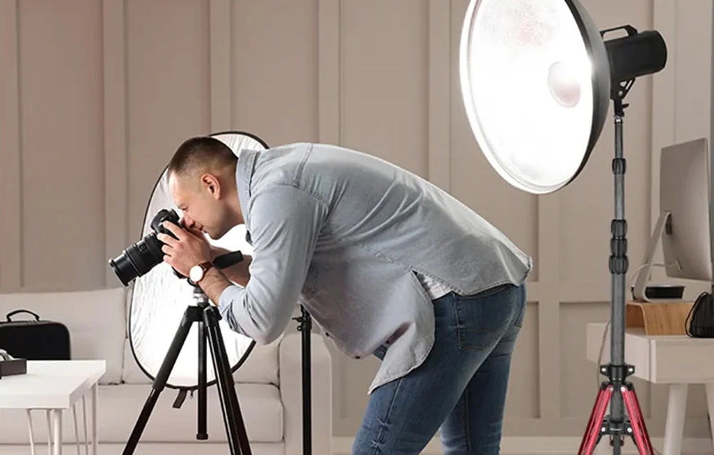 Un fotograf care lucrează într-un studio cu un aparat foto pe un trepied și o lampă de studio montată pe un stativ de iluminat