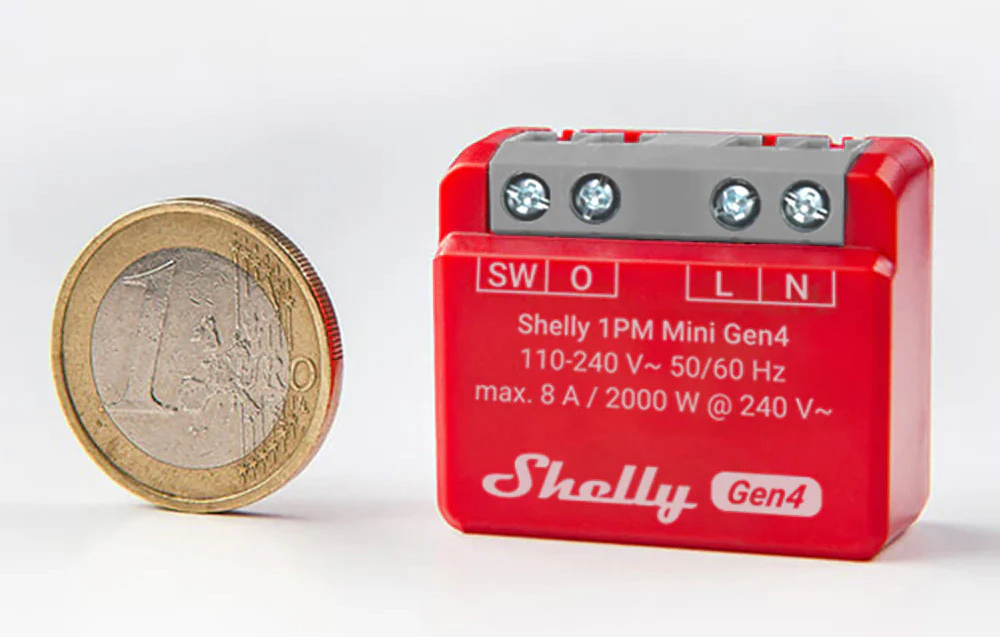 Un controler Shelly roșu așezat lângă o monedă de un euro pentru a compara dimensiunile produsului.