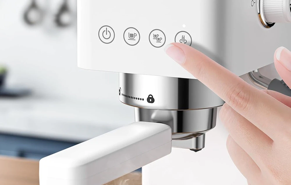 O mână apasă un buton de control tactil pe o mașină de espresso albă cu un rezervor vizibil