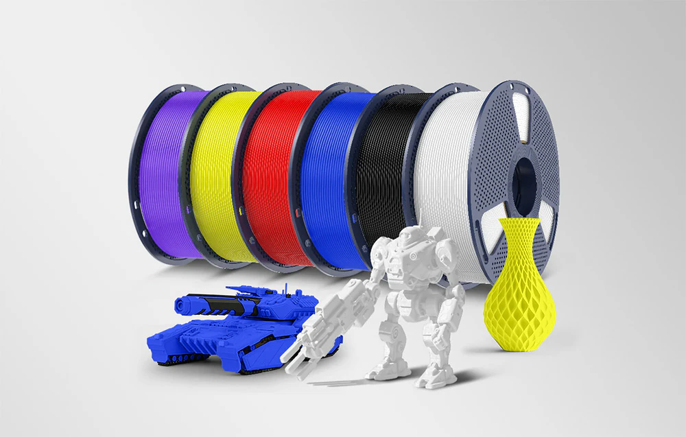 Șase role de material de imprimare colorat și modele gata realizate: un tanc albastru, un robot alb și o vază galbenă.