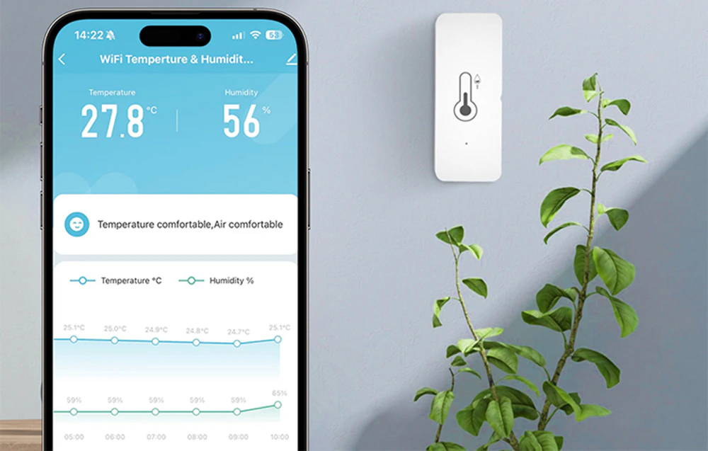 Senzor de temperatură și umiditate montat pe un perete lângă o plantă în ghiveci, cu o aplicație pentru smartphone care afișează valori de 27,8°C și 56%