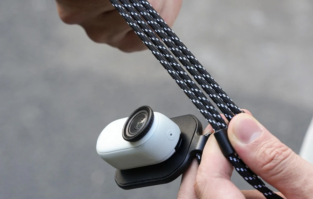 O cameră miniaturală albă atașată la un suport magnetic negru cu un cordon ținut în mâini.