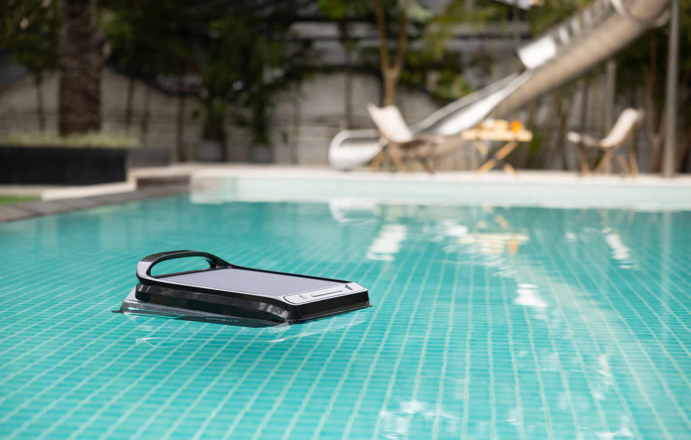 Robotul Wybot F1 plutind într-o piscină lângă o terasă cu șezlonguri