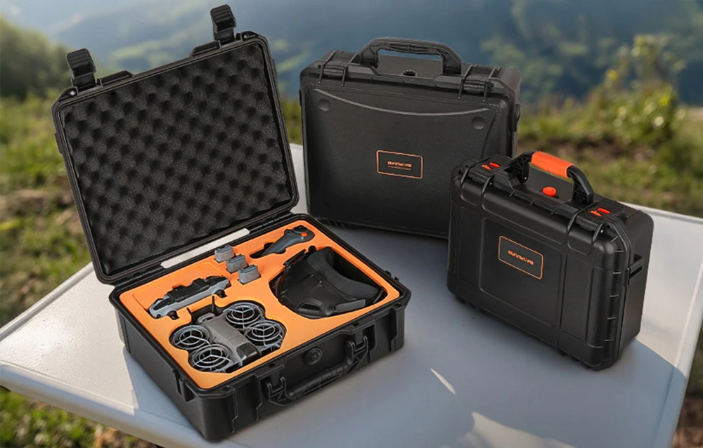 Trei valize de protecție Sunnylife, inclusiv una deschisă cu dronă și accesorii în căptușeală portocalie, pe fundalul unui peisaj muntos
