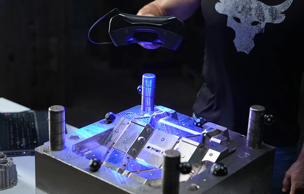 Bărbat care scanează o matriță industrială metalică cu un scaner 3D portabil care emite lumină albastră