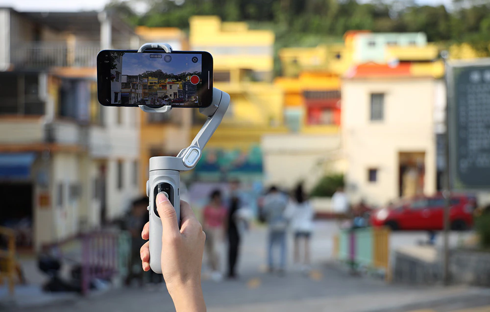 O persoană înregistrează un peisaj urban cu un smartphone montat pe un gimbal, ținând dispozitivul în mână.