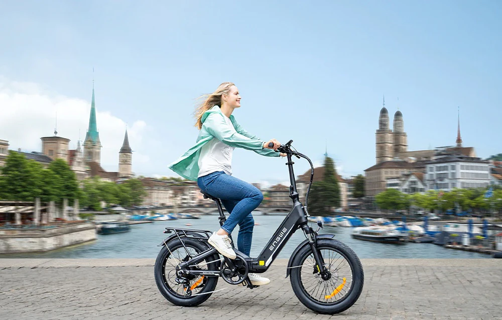 O femeie merge pe o bicicletă electrică de-a lungul malului, cu vedere spre oraș
