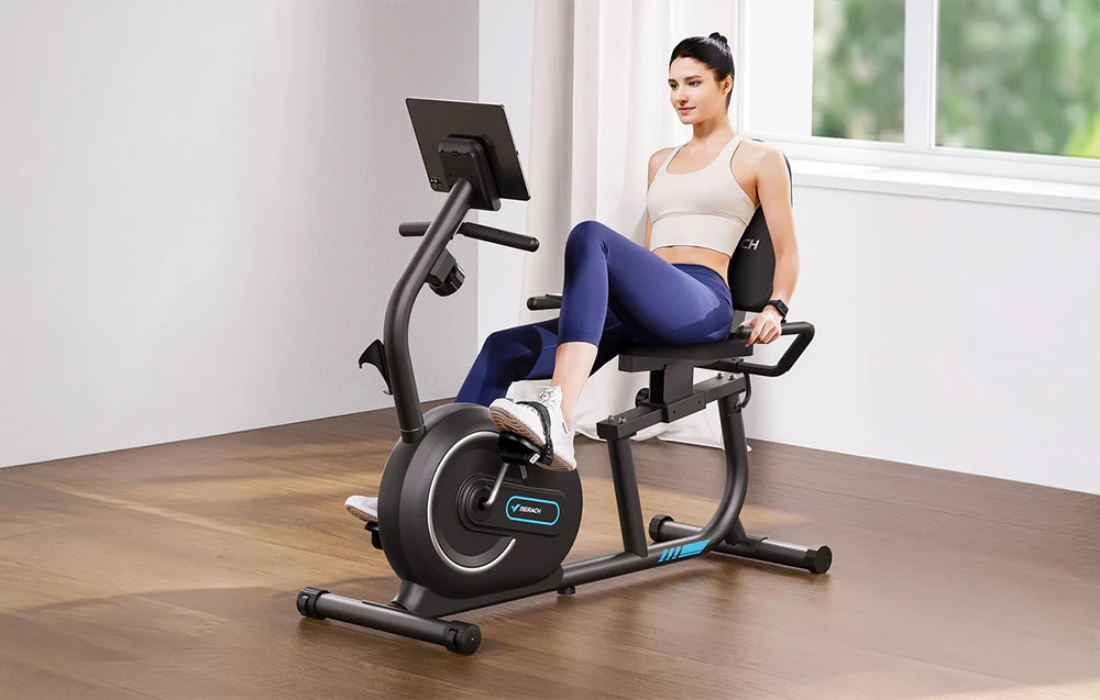Femeie care face exerciții pe o bicicletă reclinată într-o cameră curată lângă fereastră