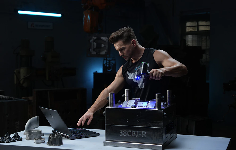 Un bărbat scanează o matriță 3D cu o mână și operează un laptop pe o masă cu cealaltă