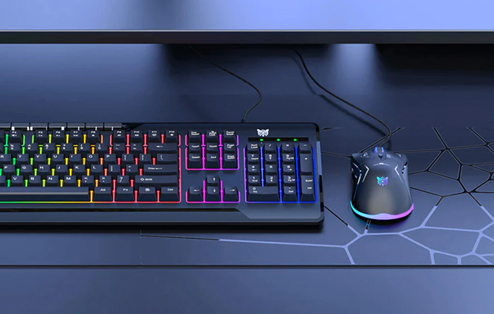 Mouse-ul de computer Onikuma se află pe birou lângă o tastatură cu iluminare de fundal