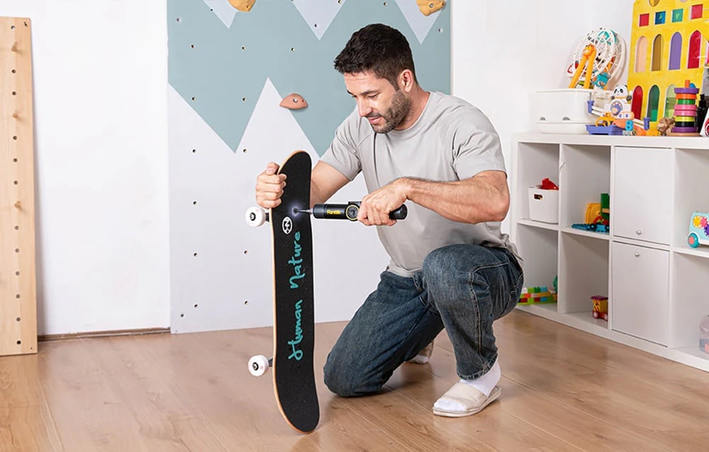 Un bărbat repară un skateboard în camera unui copil cu o șurubelniță electrică.