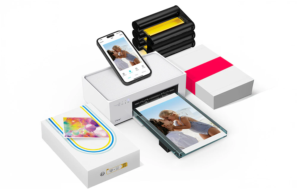 Imprimanta Liene albă înconjurată de accesorii: cartușe de cerneală, hârtie foto și un smartphone cu o fotografie finalizată.