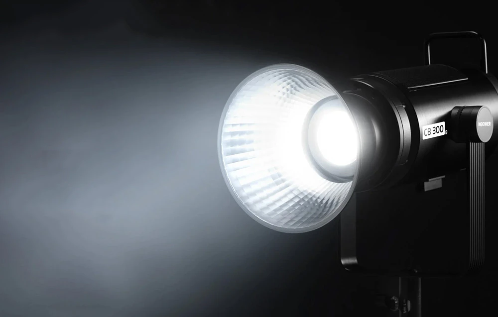 O lampă modernă de studio cu abajur argintiu, care emite un fascicul puternic de lumină albă și strălucitoare.