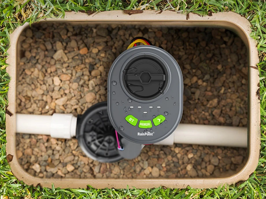 Controler RainPoint într-o cutie mică cu valve umplută cu pietricele, vedere de sus.