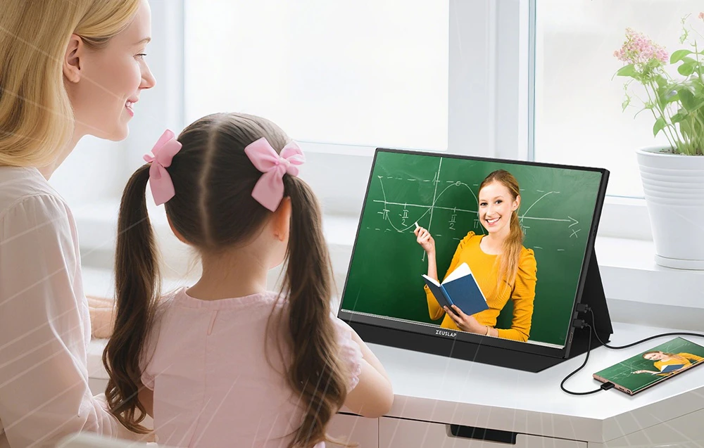 O mamă și fiica ei urmăresc o lecție online pe un monitor ZEUSLAP conectat prin cablu la un smartphone așezat pe un birou alb