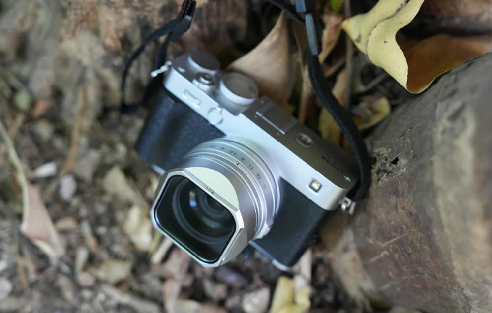 Cameră foto Fujifilm cu accesorii Freewell așezată pe solul pădurii lângă un trunchi de copac
