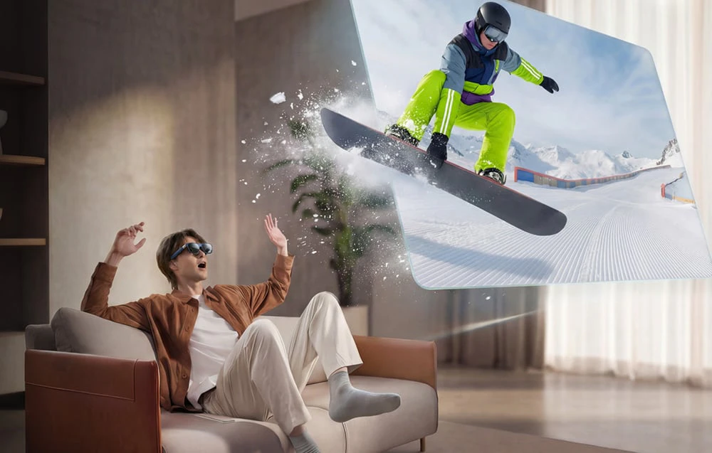 Un bărbat care poartă ochelarii AR stă pe o canapea; în dreapta, este afișată imaginea unei persoane pe o placă de snowboard