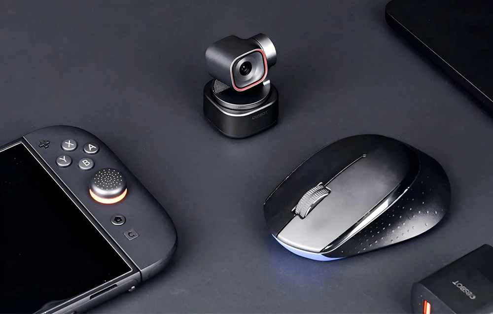 Camera OBSBOT pe o bază rotativă așezată pe un birou lângă o telecomandă și un mouse de computer