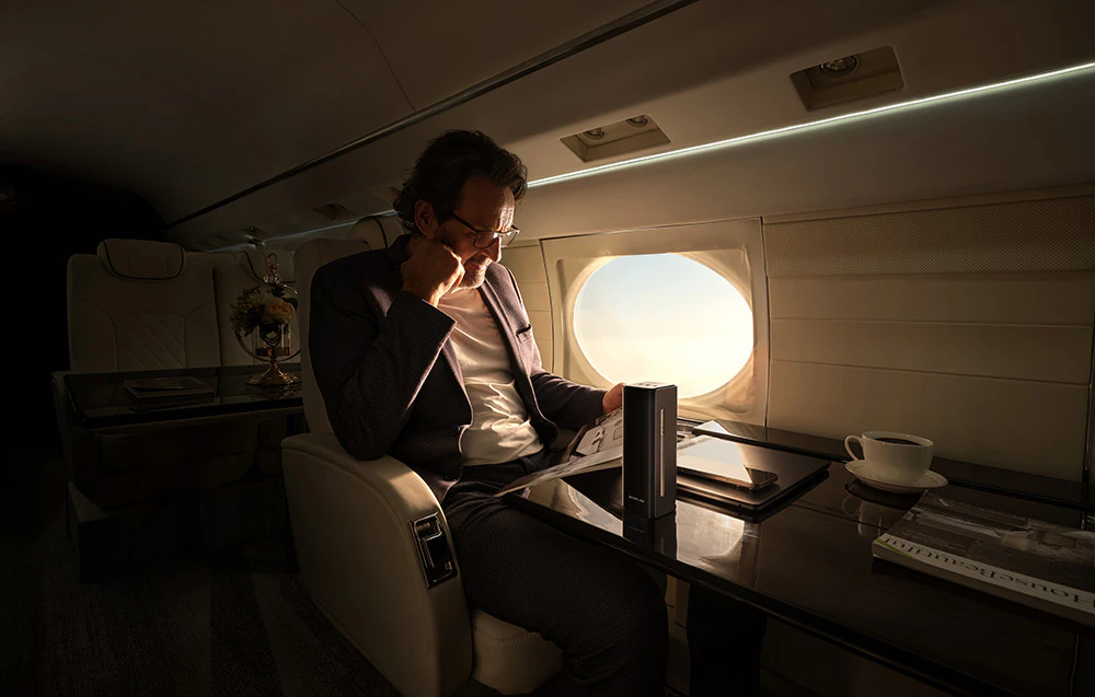 Un bărbat în costum lucrează la un laptop în cabina unui avion privat lângă o fereastră.