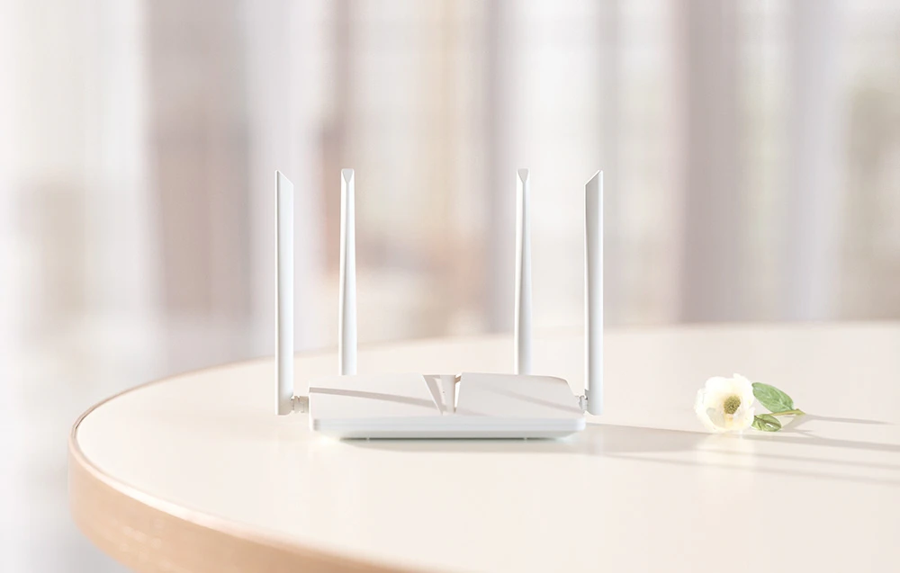 Un router Wi-Fi alb cu patru antene așezat pe o masă rotundă de culoare deschisă, lângă o floare albă, pe un fundal interior estompat