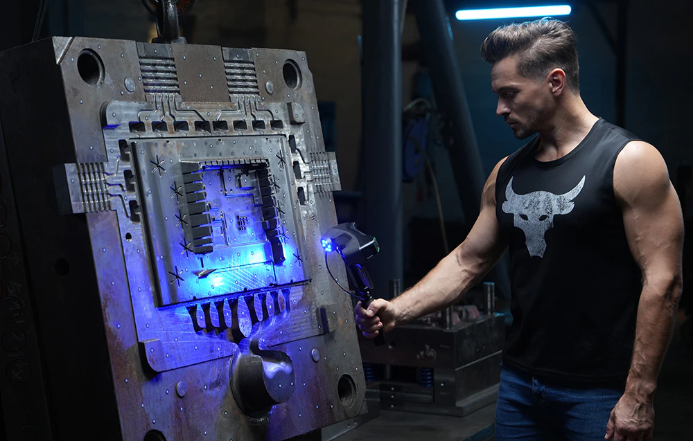 Un bărbat scanează o formă industrială verticală mare cu un scaner 3D care emite lumină albastră