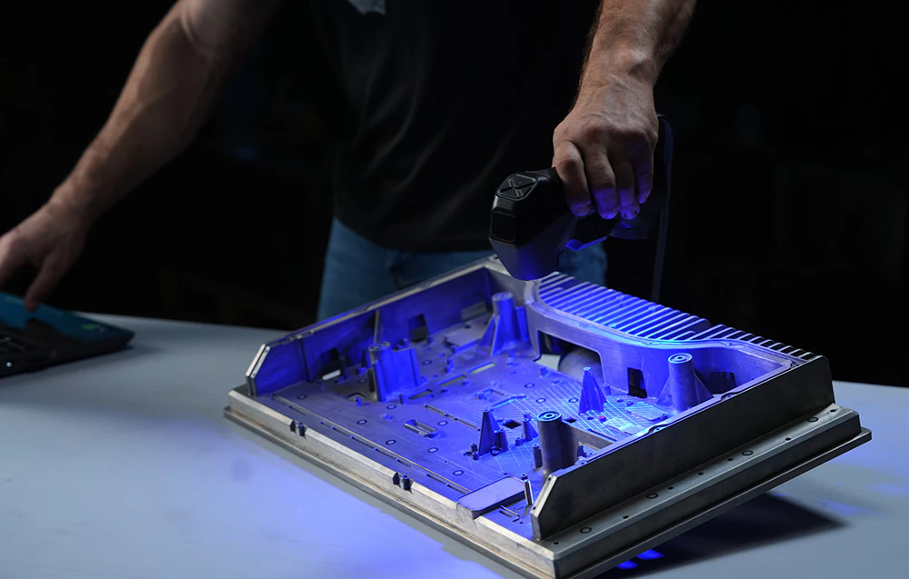 Prim plan al mâinii unui bărbat care scanează o piesă metalică cu lumina albastră a scanerului 3D