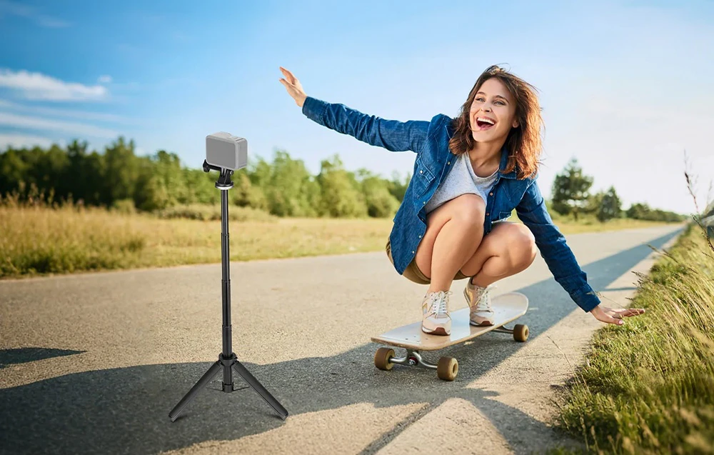O fată pe un skateboard trece pe lângă o cameră de acțiune montată pe un trepied înalt lângă drum.