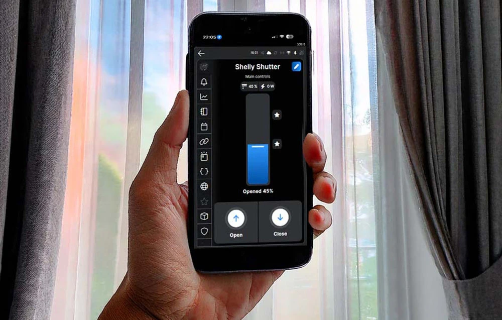 Smartphone cu aplicația Shelly Shutter, care afișează jaluzelele setate la 45% deschidere, pe fundalul unei ferestre cu perdele