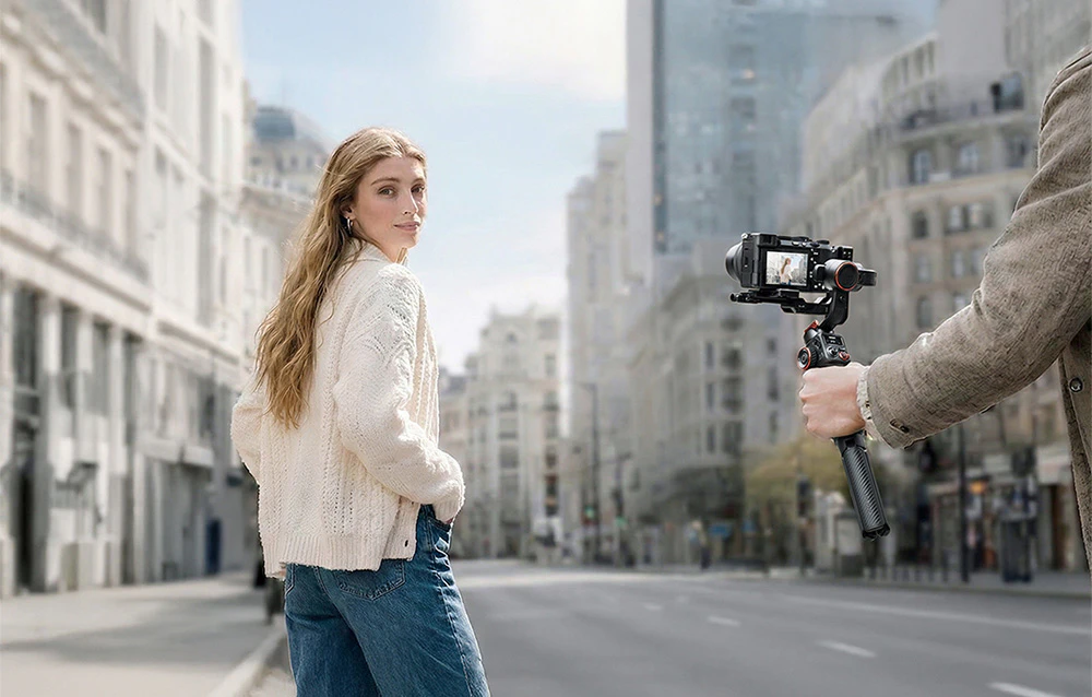 O persoană cu un gimbal și o cameră care filmează o fată pe o stradă din oraș