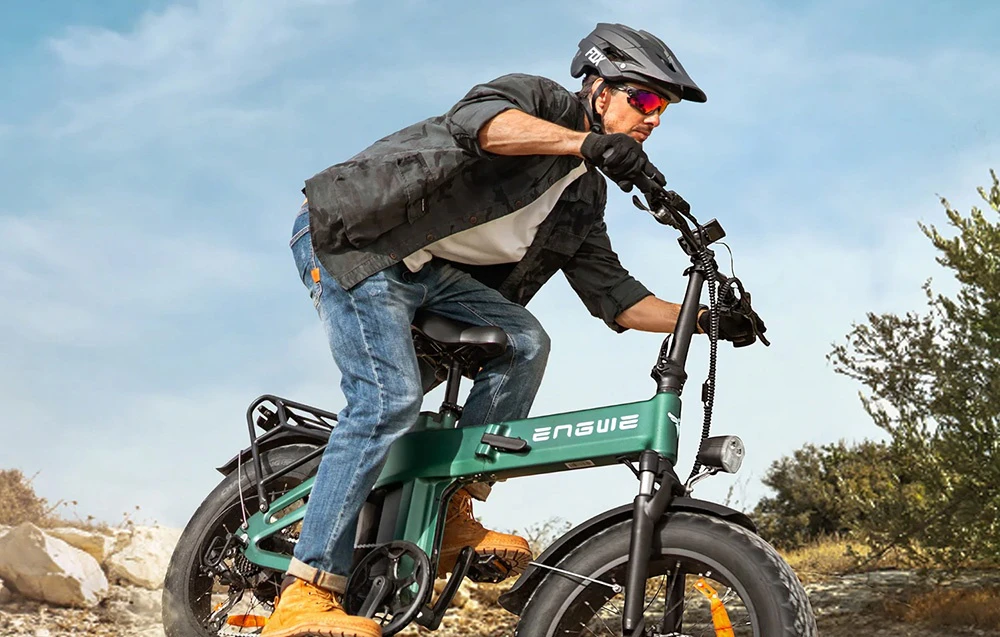 Un bărbat care poartă cască conduce o bicicletă electrică pliabilă verde pe un drum pietruit