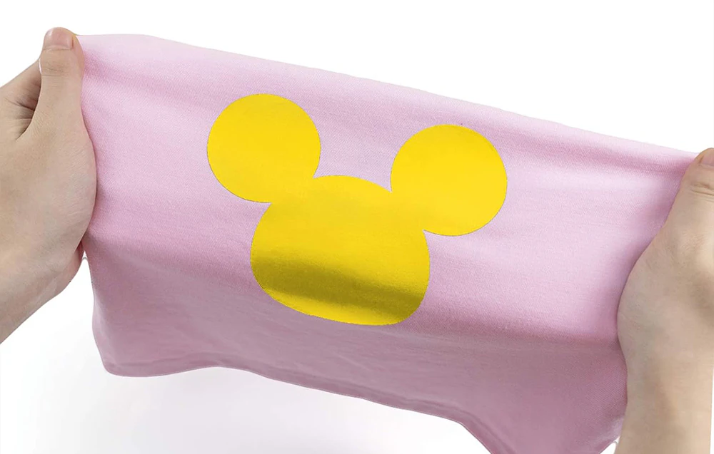 Autocolant galben cu Mickey Mouse pe un tricou roz ținut în mâini