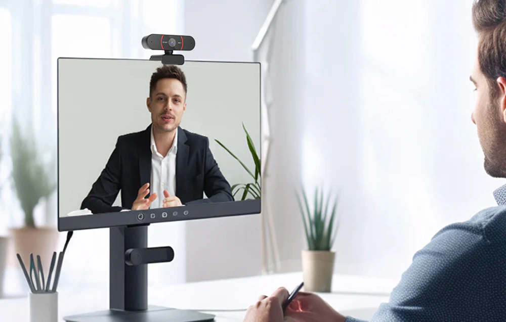 Un bărbat care efectuează un apel video prin intermediul unei camere montate pe monitorul unui computer.