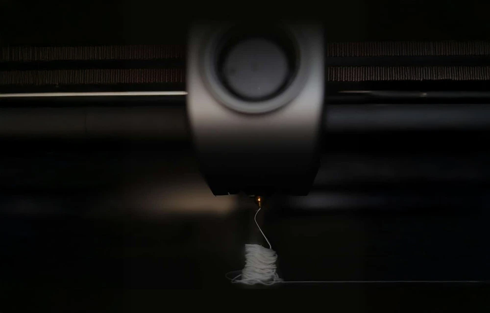 Un prim plan al duzei unei imprimante 3D care imprimă filament alb pe un fundal închis