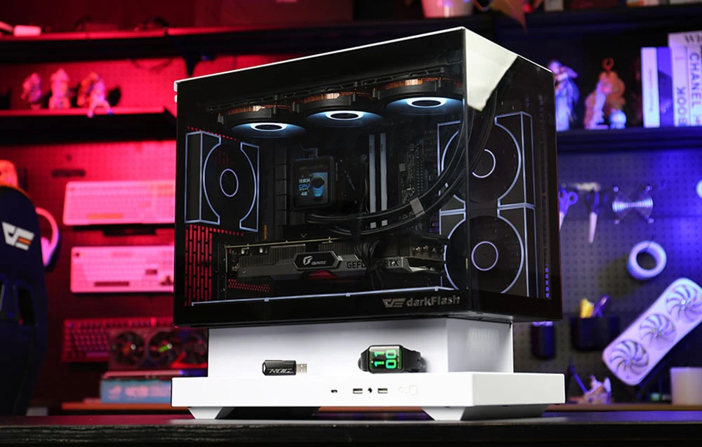 Carcasă de computer cu panouri transparente și bază albă pe fundalul unui atelier cu iluminare colorată